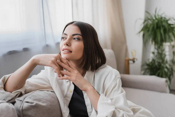 Tattooed young woman looking away on couch at home — Stock Photo
