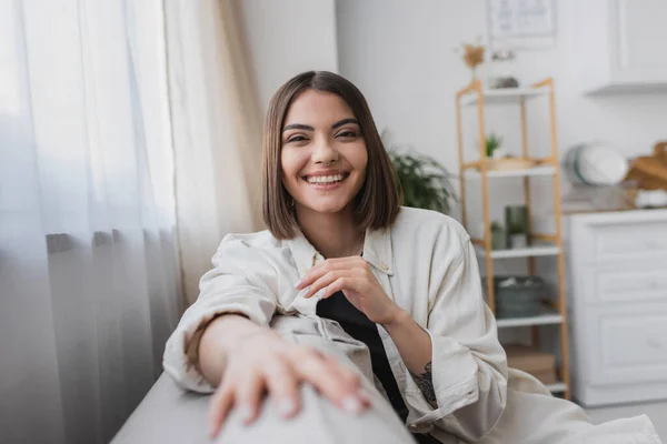 Carefree young woman looking at camera while sitting on couch at home — Stock Photo