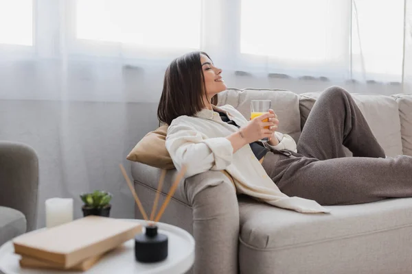 Вид збоку задоволена жінка тримає склянку апельсинового соку на дивані вдома — стокове фото