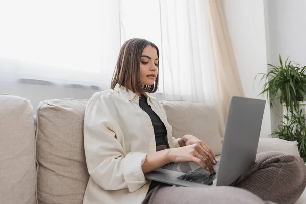 Young brunette freelancer using laptop on couch in living room — Stock Photo
