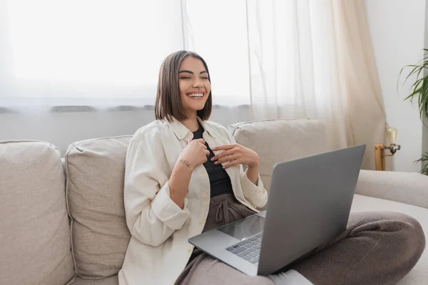 Positiv tätowierte Frau hält Laptop, während sie zu Hause auf der Couch sitzt — Stockfoto