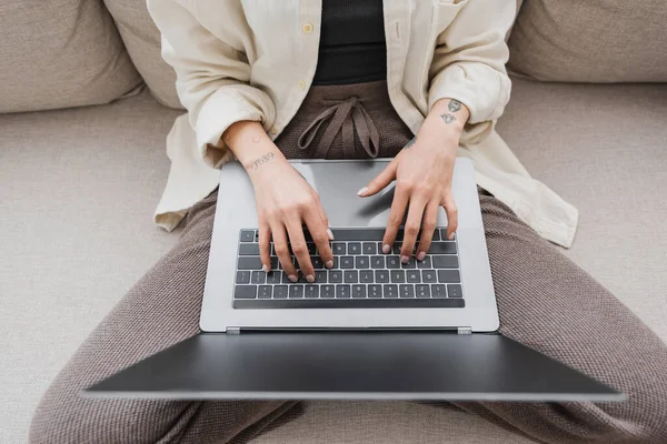 Top view of tattooed freelancer using laptop with blank screen on couch in living room — Stock Photo