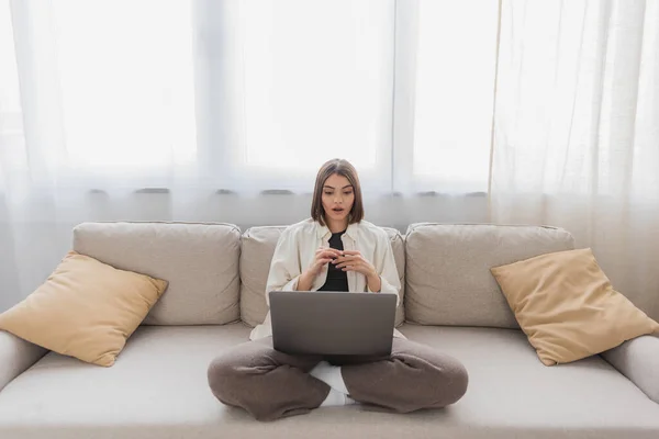 Geschockte Freiberuflerin schaut auf Laptop auf Couch im Wohnzimmer — Stockfoto