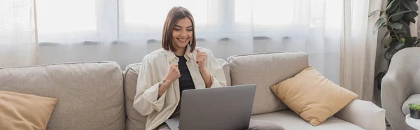 Young freelancer showing yes gesture near laptop on couch at home, banner — Stock Photo