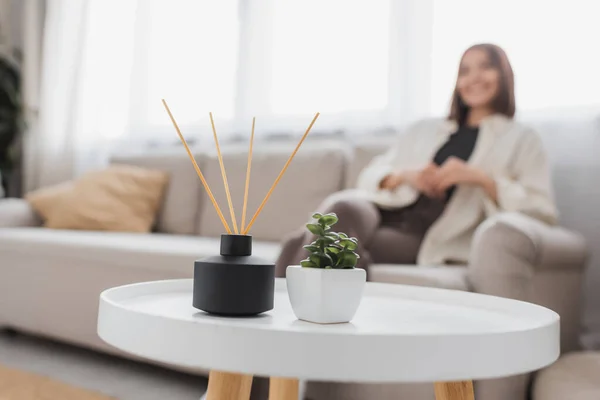 Bastoncini di aroma di bambù e pianta sul tavolino vicino alla donna offuscata a casa — Foto stock