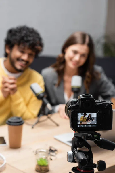 Fokus auf professionelle Digitalkameraaufnahmen verschwommen und glücklich interracial Podcasters in der Nähe von professionellen Mikrofonen und Kaffee auf den Tisch im Radiostudio gehen — Stockfoto