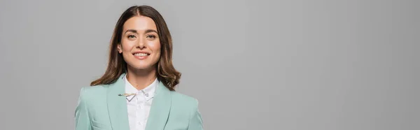 Portrait of cheerful brunette host of event in blue formal wear looking at camera during holiday while standing isolated on grey with copy space, banner — Stock Photo