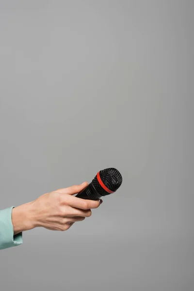 Ausgeschnittene Ansicht eines schwarzen drahtlosen Mikrofons in der Hand des Veranstalters in grüner Jacke während eines Auftritts im Urlaub, während er isoliert auf grau steht — Stockfoto