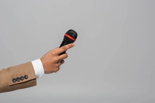 Ausgeschnittene Ansicht der Hand des Veranstalters in brauner Jacke mit Mikrofon während des Auftritts, während er isoliert auf grau steht — Stockfoto