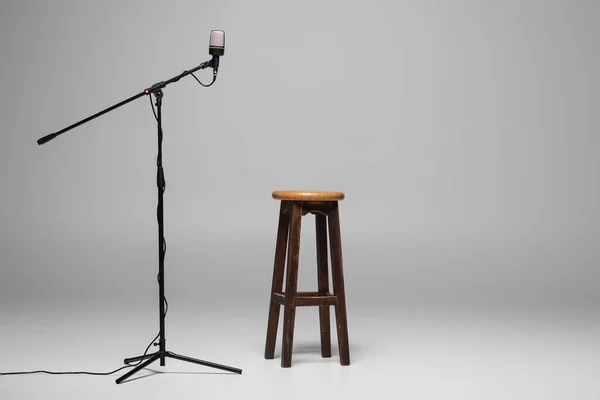 Sedia in legno marrone in piedi vicino al microfono con filo su supporto su sfondo grigio con spazio copia, sgabello alto in studio — Foto stock
