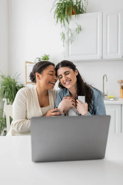 Cheerful interracial lgbt couple holding hands and smiling during video call — Stock Photo