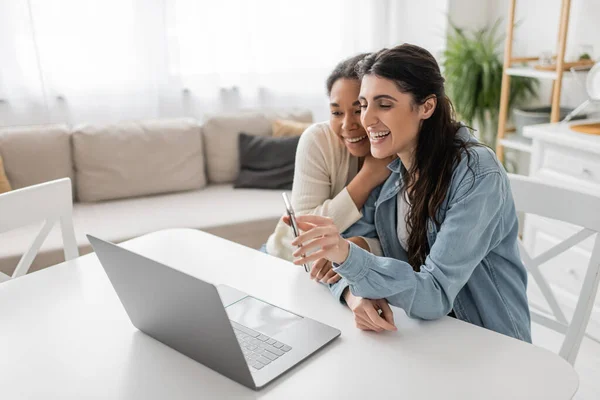 Heureuse lesbienne femme montrant smartphone pendant appel vidéo tout en étant assis à côté de petite amie — Photo de stock