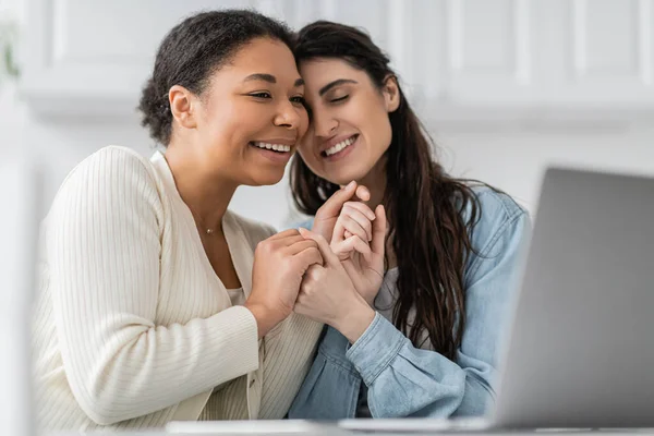 Pleased interracial lesbian couple holding hands near laptop — Stock Photo