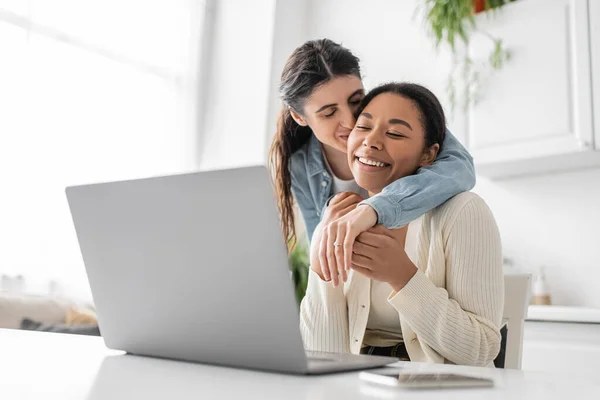 Fröhliches multiethnisches lesbisches Paar zeigt Verlobungsring bei Videoanruf auf Laptop — Stockfoto