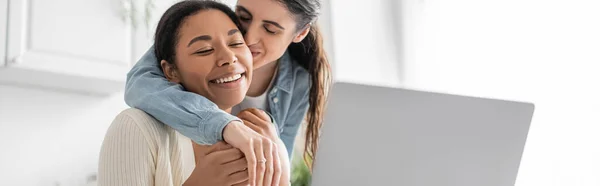 Fröhliches multiethnisches lesbisches Paar zeigt Verlobungsring während Videoanruf auf Laptop, Banner — Stockfoto