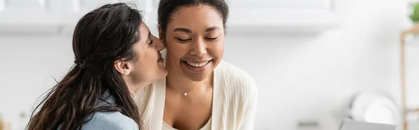 Happy lesbian woman kissing cheek of cheerful multiracial girlfriend, banner — Stock Photo