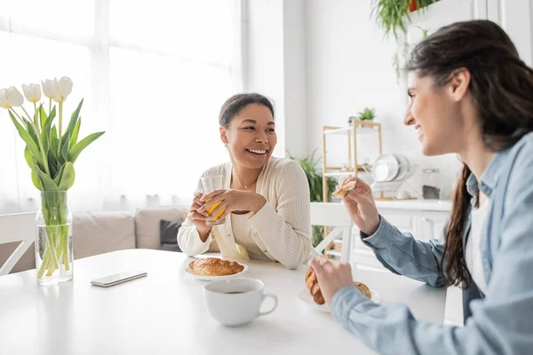 Feliz multirracial lgbt casal sorrindo enquanto tendo café da manhã na cozinha — Fotografia de Stock
