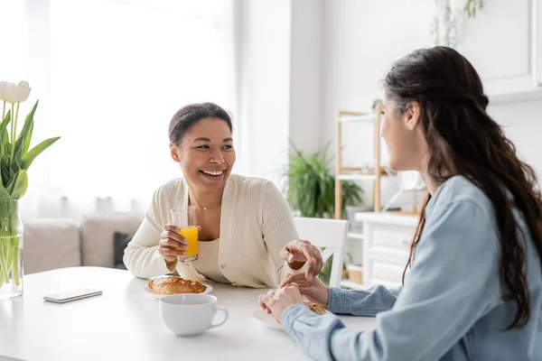 Весёлая многорасовая лесбийская пара улыбается во время завтрака на кухне — стоковое фото