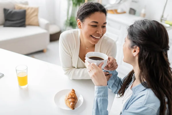 Overhead view of cheerful multiracial lesbian couple smiling during breakfast in kitchen — Stock Photo