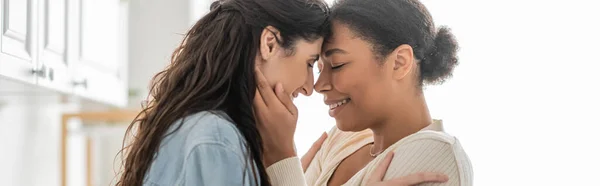 Curly multiracial woman hugging cheerful girlfriend with closed eyes at home, banner — Stock Photo
