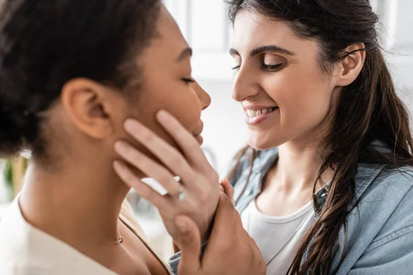 Обрученная лесбиянка с обручальным кольцом, улыбающаяся и обнимающая многорасового партнера — стоковое фото