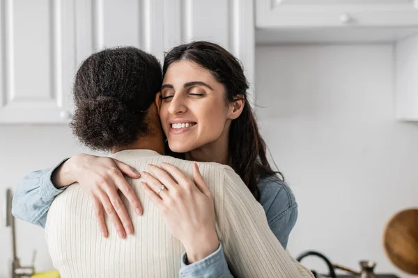 Overjoyed lesbian woman with wedding ring on finger smiling and hugging multiracial girlfriend — Stock Photo