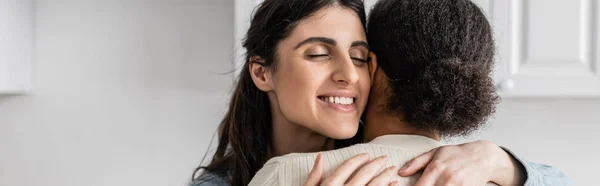 Overjoyed lesbian woman smiling and hugging multiracial girlfriend with curly hair, banner — Stock Photo