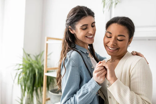 Überglückliche lesbische Frau lächelt, während sie den Verlobungsring ihrer multirassischen Freundin mit lockigem Haar betrachtet — Stockfoto