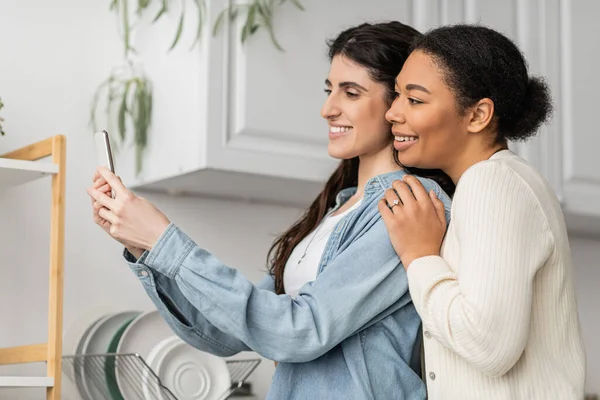 Overjoyed lesbian woman taking selfie with happy multiracial girlfriend — Stock Photo