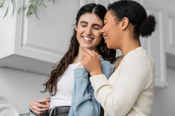 Overjoyed multiracial woman with engagement ring on finger hugging with girlfriend — Stock Photo