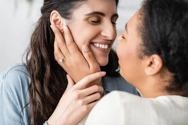 Felice donna multirazziale con anello di fidanzamento su dito abbracciando sorridente fidanzata — Foto stock