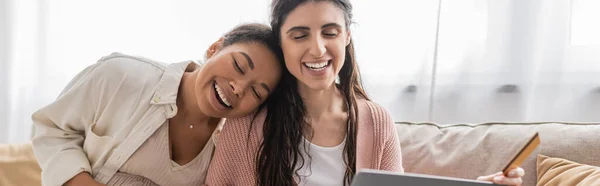 Gai lesbienne femme tenant carte de crédit près heureux multiracial partenaire, bannière — Photo de stock