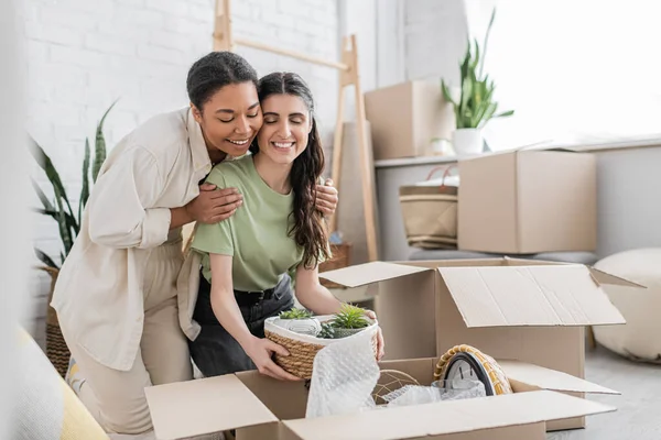 Fröhliche multirassische Frau umarmt Schultern einer glücklichen Freundin beim Umzug in ein neues Haus — Stockfoto