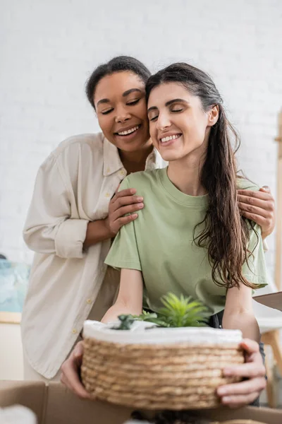 Joyful multiracial woman hugging shoulders of happy girlfriend while moving to new house — Stock Photo