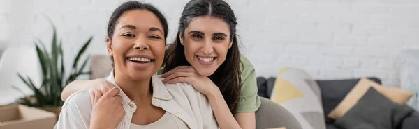 Freudige lesbische Frau umarmt glücklich multirassische Freundin im Wohnzimmer, Banner — Stockfoto