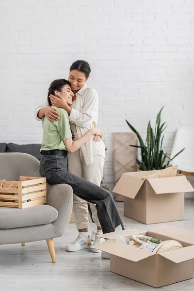 Glückliche lesbische Frau umarmt freudige multirassische Freundin mit geschlossenen Augen im Wohnzimmer des neuen Hauses — Stockfoto