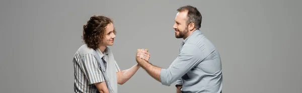 Visão lateral do pai feliz e do filho adolescente apertando as mãos isoladas no cinza, banner — Fotografia de Stock
