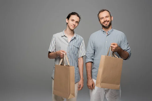 Happy teenage boy and dad holding shopping bags isolated on grey — Stock Photo