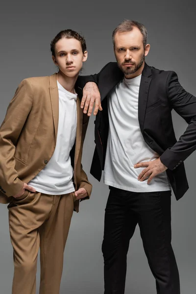 Selbstbewusster Vater und Teenager-Sohn in Anzügen posieren gemeinsam isoliert auf grau — Stockfoto