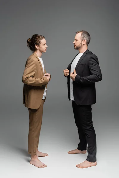 Full length of well dressed father and son adjusting blazers and looking at each other on grey — Stock Photo