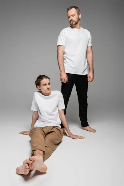 Vater blickt seinen halbwüchsigen Sohn in weißem T-Shirt auf grau an — Stockfoto