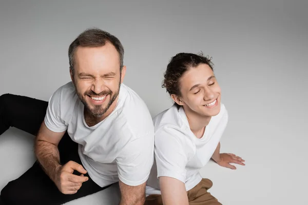 Overhead view of cheerful father and teenage son in white t-shirts smiling on grey — Stock Photo