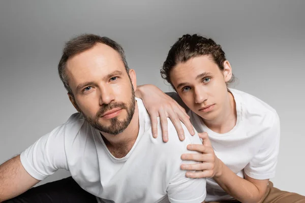 Bearded man with his teenage son looking at camera isolated on grey — Stock Photo