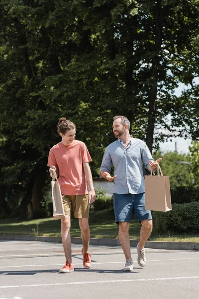Весёлый папа и счастливый сын-подросток гуляют с сумками на улице — стоковое фото