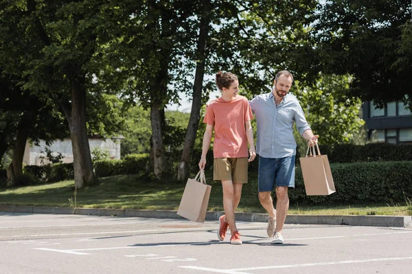 Bärtiger Vater und glücklicher Teenager-Sohn spazieren mit Einkaufstüten im Freien — Stockfoto