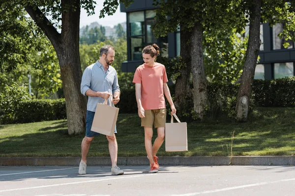 Pai barbudo e filho adolescente andando com sacos de compras ao ar livre — Fotografia de Stock