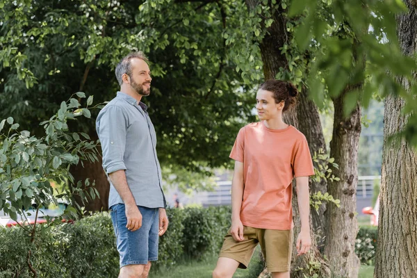 Cheerful teenage boy looking at happy father in green park — Stock Photo
