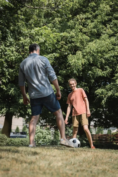 Щасливий хлопчик-підліток грає у футбол з батьком у зеленому літньому парку — стокове фото