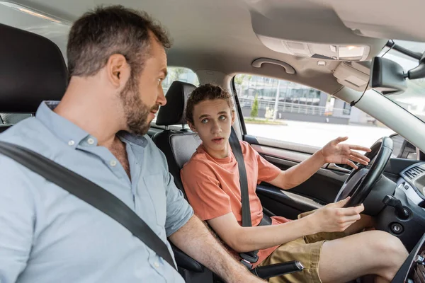 Teenaged boy sitting next to dad while learning how to drive car — Stock Photo