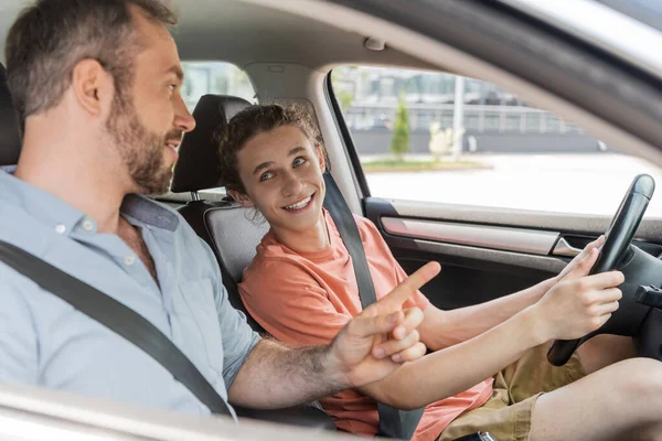 Happy teenaged boy sitting next to dad while learning how to drive car — Stock Photo